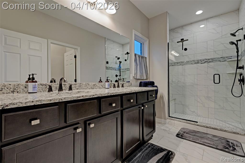 Full bath featuring double vanity, a stall shower, light marble finish floors, and recessed lighting