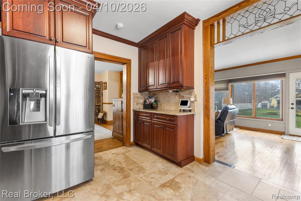 Kitchen featuring stainless steel refrigerator with ice dispenser, crown molding, light stone countertops, and decorative backsplash