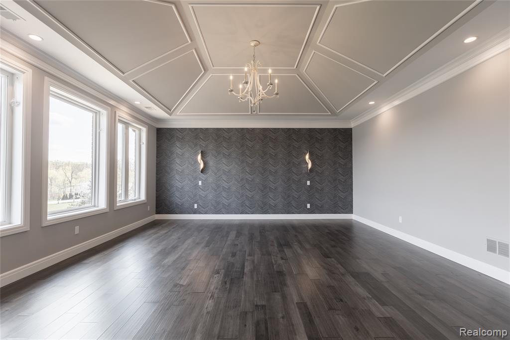 Spare room featuring an accent wall, suspended lighting, wallpapered walls, dark wood-style flooring, and ornamental molding
