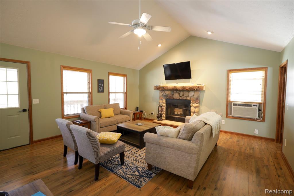 Living area featuring ceiling fan, hardwood / wood-style floors, a stone fireplace, and cooling unit