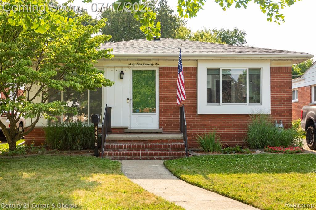 Brick exterior residence featuring a front yard with mature trees and a concrete pathway