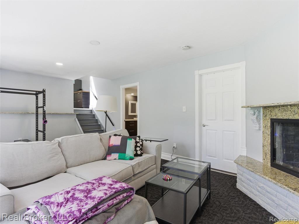 Living area featuring a fireplace with a light-colored stone surround and white brick hearth, recessed ceiling lighting, and a six-panel interior door
