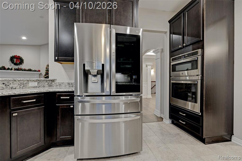 Kitchen featuring stainless steel appliances, light stone countertops, arched walkways, dark wood finish cabinetry, and recessed lighting