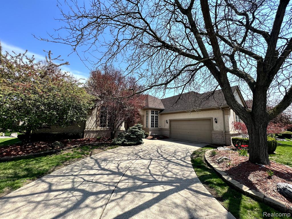 Stucco exterior residence featuring a curved concrete driveway, integrated two-car garage, and a bay window with architectural grilles