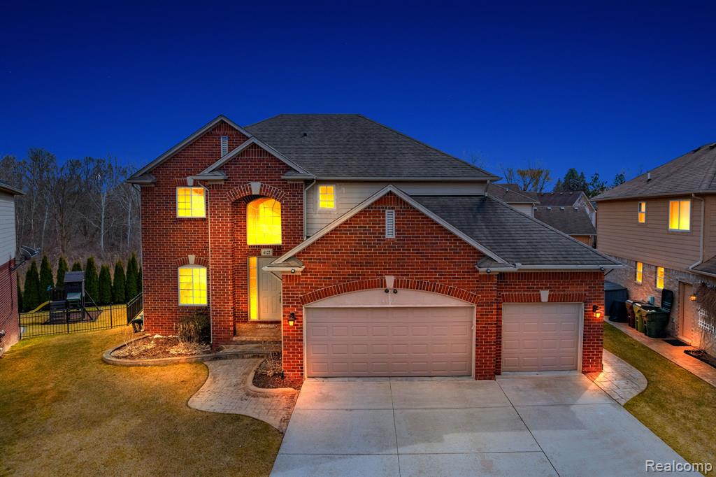 Traditional-style house featuring a garage, driveway, brick siding, and roof with shingles