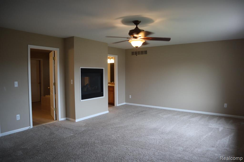 Unfurnished living room featuring carpet floors, ceiling fan, and a warm lit fireplace