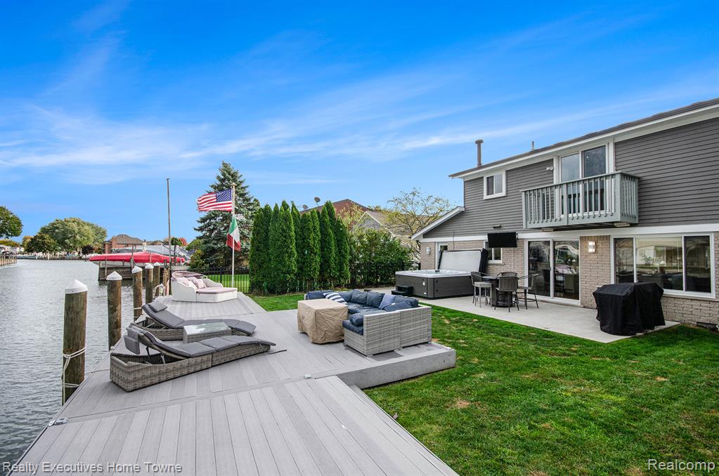 Dock area with a hot tub, a patio area, a water view, and a yard