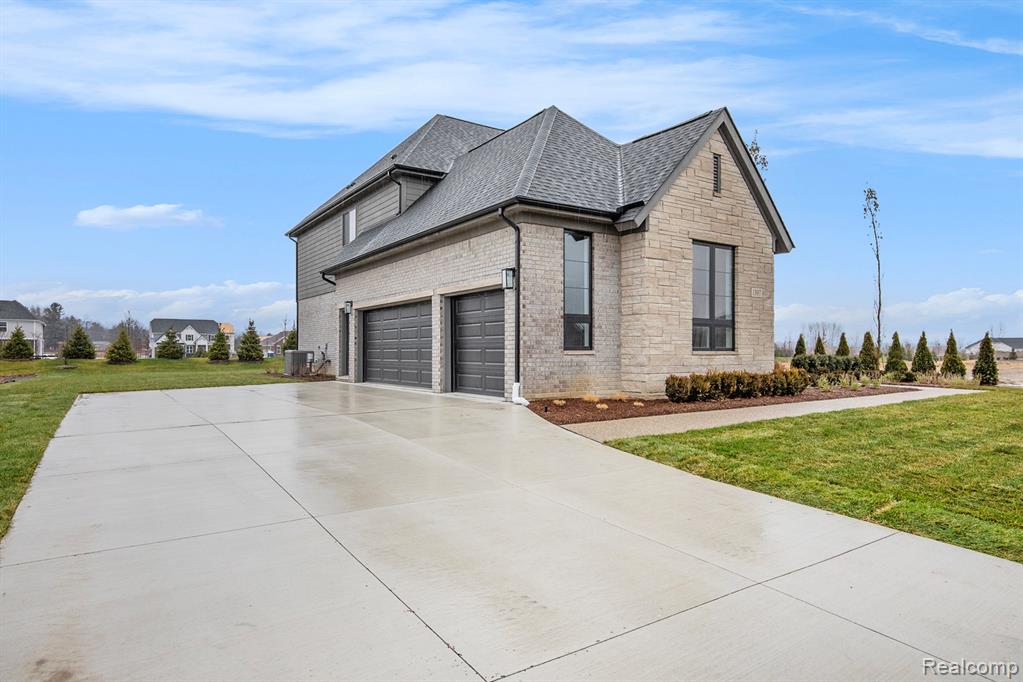 View of side of property featuring a yard, concrete driveway, stone siding, and a shingled roof