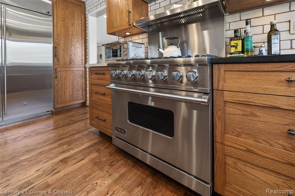 Kitchen with wood finish cabinetry, high quality appliances, dark wood finished floors, and decorative backsplash