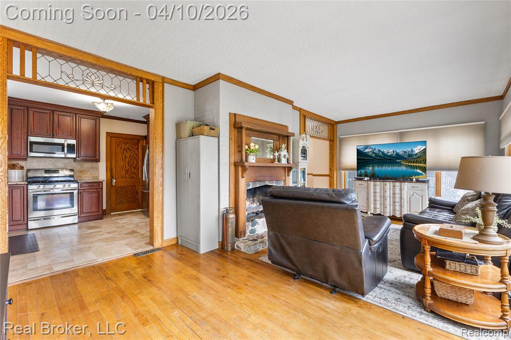 Living area with crown molding, light wood finished floors, and a fireplace with raised hearth