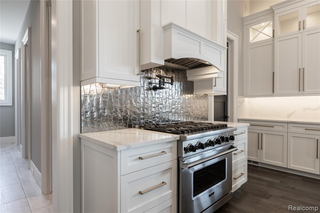 Kitchen featuring white cabinets, stainless steel stove, light stone countertops, and decorative backsplash