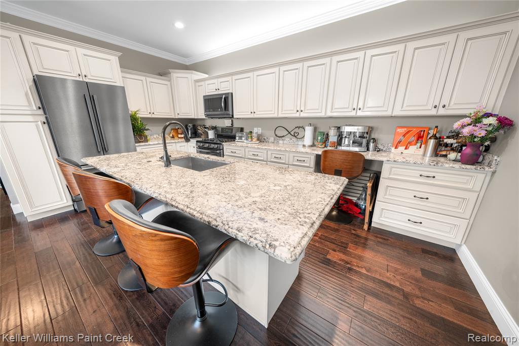 Kitchen with a breakfast bar, stainless steel appliances, dark wood-style flooring, light stone counters, and a kitchen island with sink