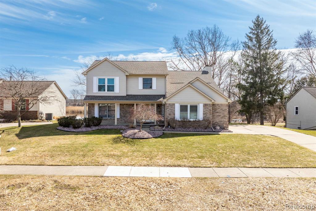 Traditional-style house with a porch, a front lawn, brick siding, a shingled roof, and driveway