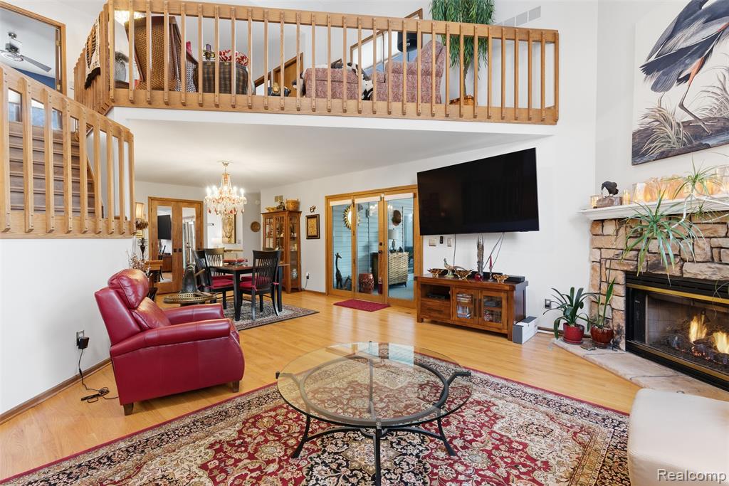 Living area featuring wood finished floors, a high ceiling, a stone fireplace, and suspended lighting