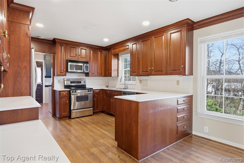 Kitchen with stainless steel appliances, light countertops, wood finish cabinetry, recessed lighting, and crown molding