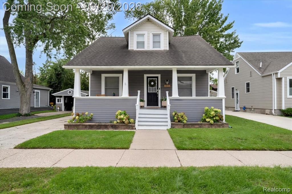 Gray siding exterior with white trim, covered front porch, concrete sidewalk, and a manicured lawn