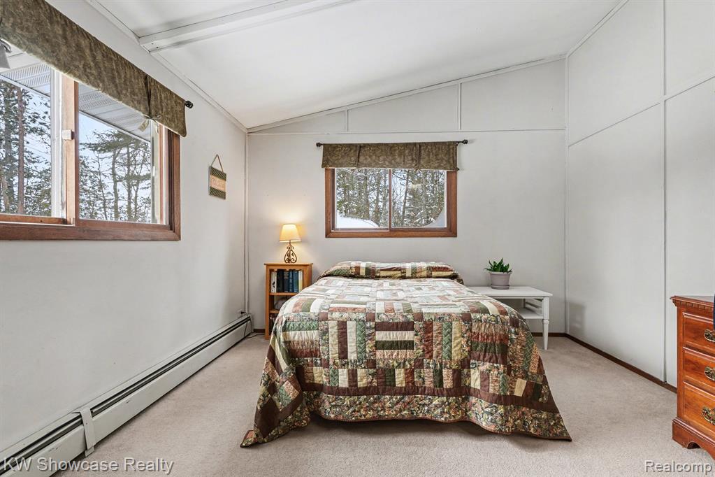 Bedroom featuring baseboard heating, vaulted ceiling, and light carpet