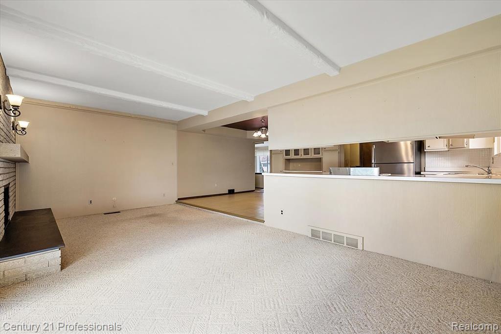 Unfurnished living room with beam ceiling, a chandelier, a fireplace with raised hearth, and light carpet