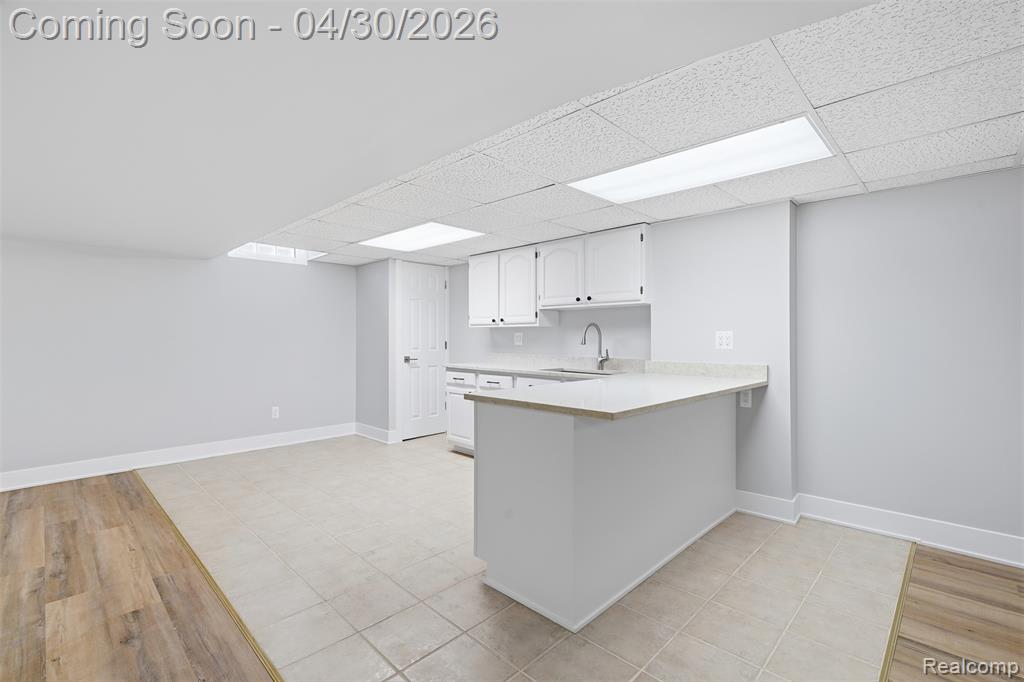 Kitchenette with light countertops, a peninsula, a paneled ceiling, and white cabinets
