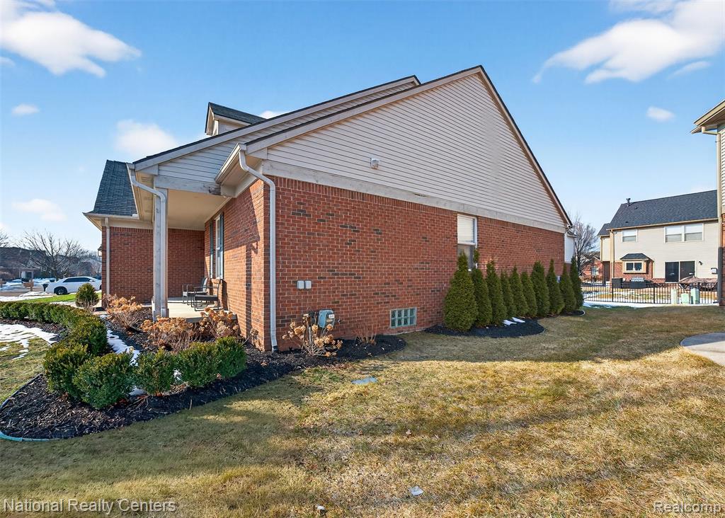 View of property exterior featuring a lawn, brick siding, and a patio area