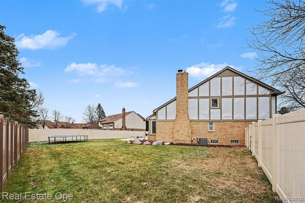 Back of house with a fenced backyard, a chimney, a trampoline, and brick siding