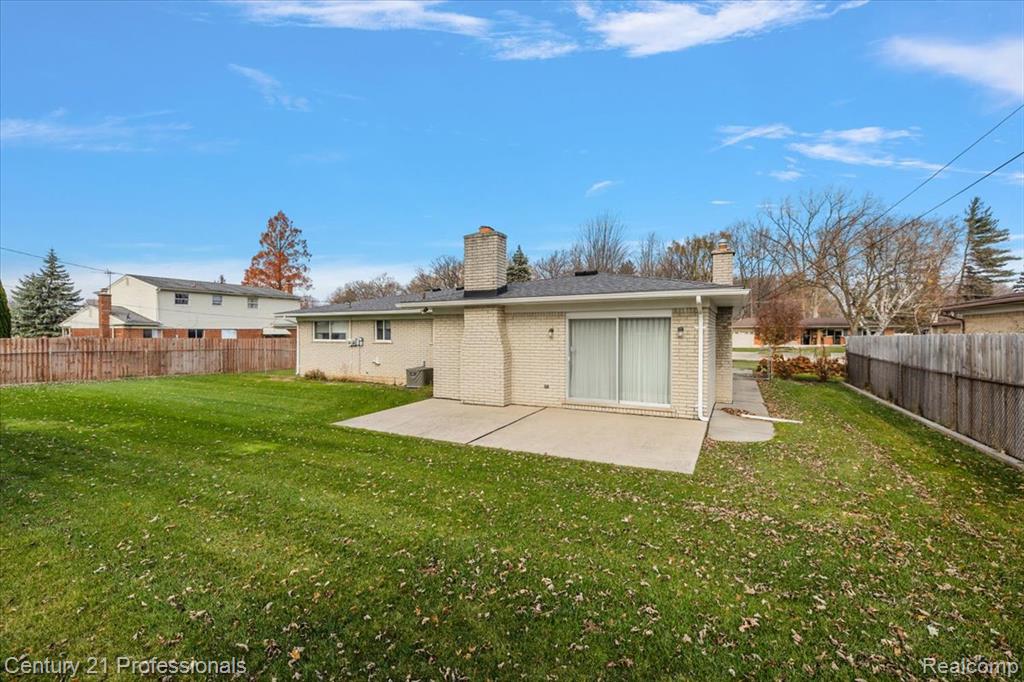 Rear view of house featuring a patio, brick siding, a fenced backyard, and a chimney