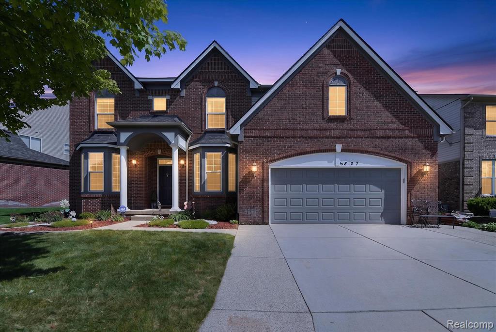 Brick exterior residence featuring a front porch with white columns, dual bay windows, an attached two-car garage, and manicured landscaping