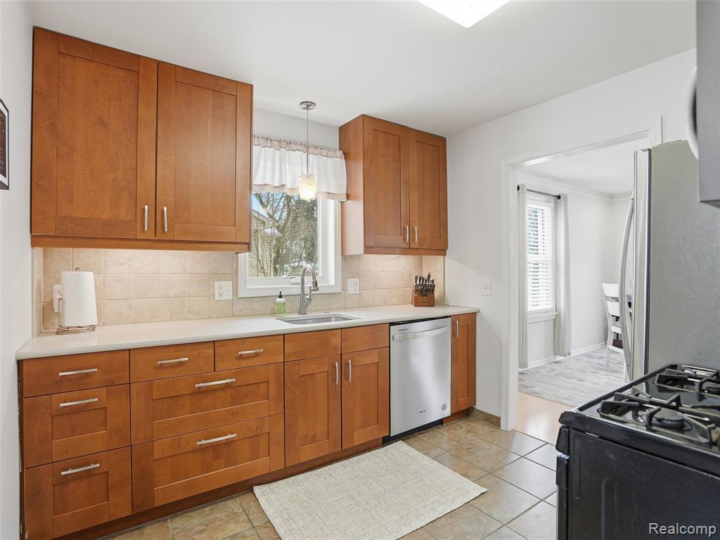 Kitchen featuring wood finish cabinetry, backsplash, stainless steel appliances, decorative light fixtures, and light stone countertops