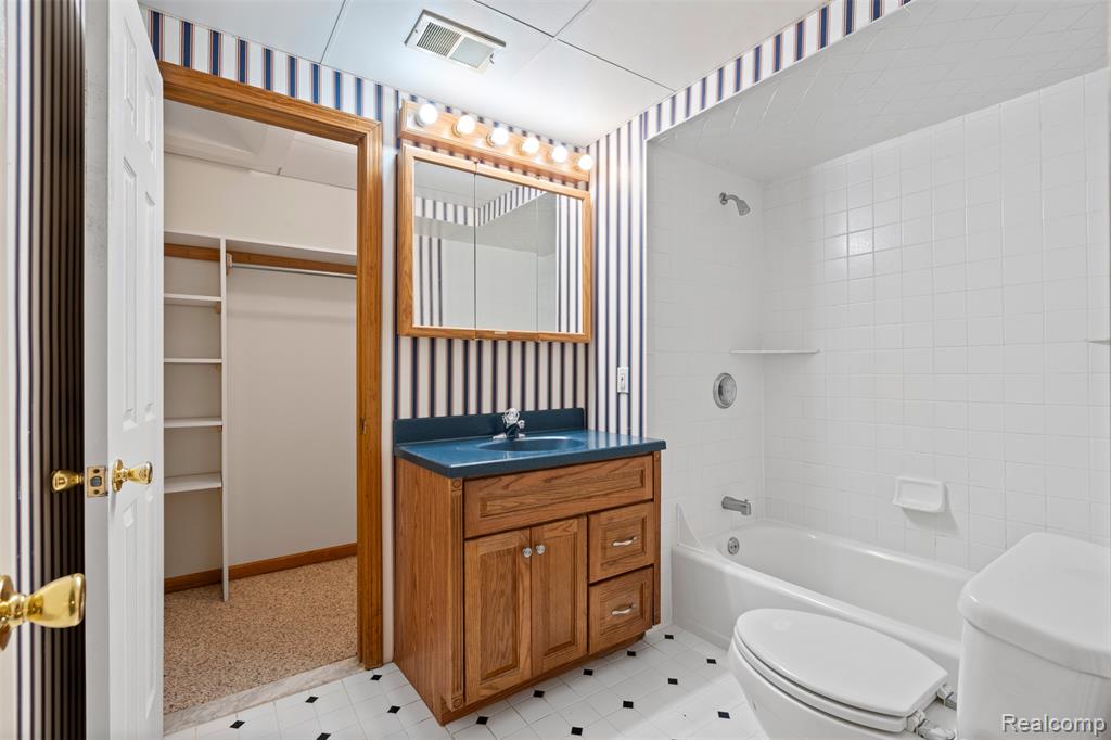 Bathroom with tub / shower combination, vanity, wallpapered walls, a walk in closet, and light floors