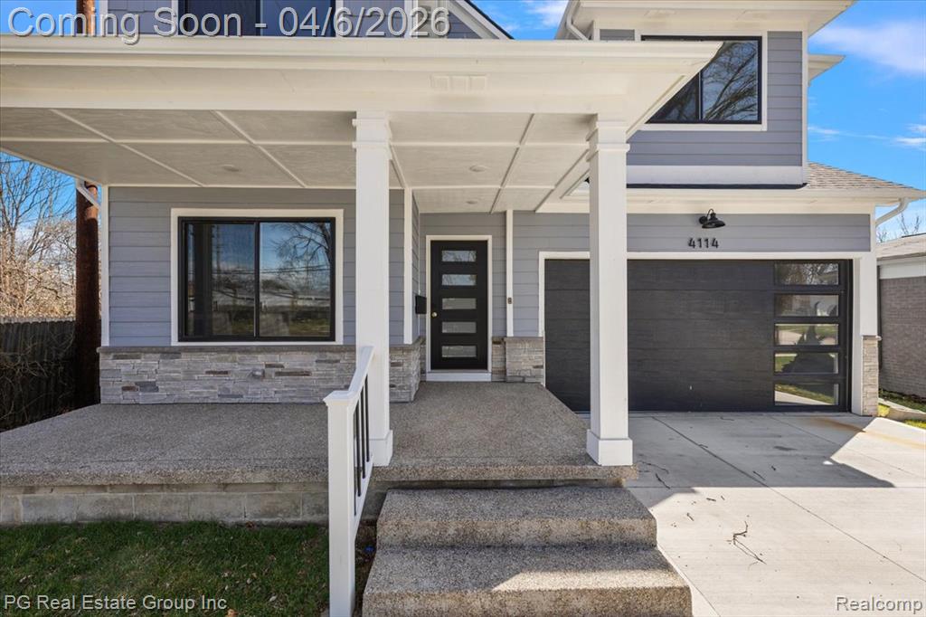 View of exterior entry featuring a porch, stone siding, concrete driveway, and a garage