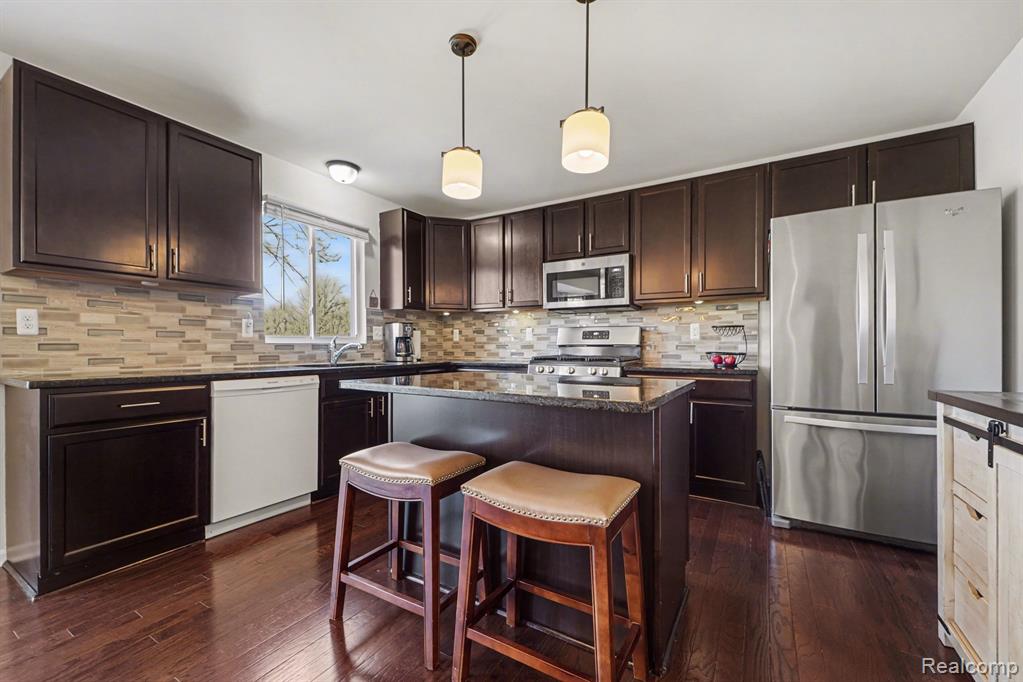 Kitchen with dark wood finish cabinets, stainless steel appliances, a kitchen island, and dark stone countertops