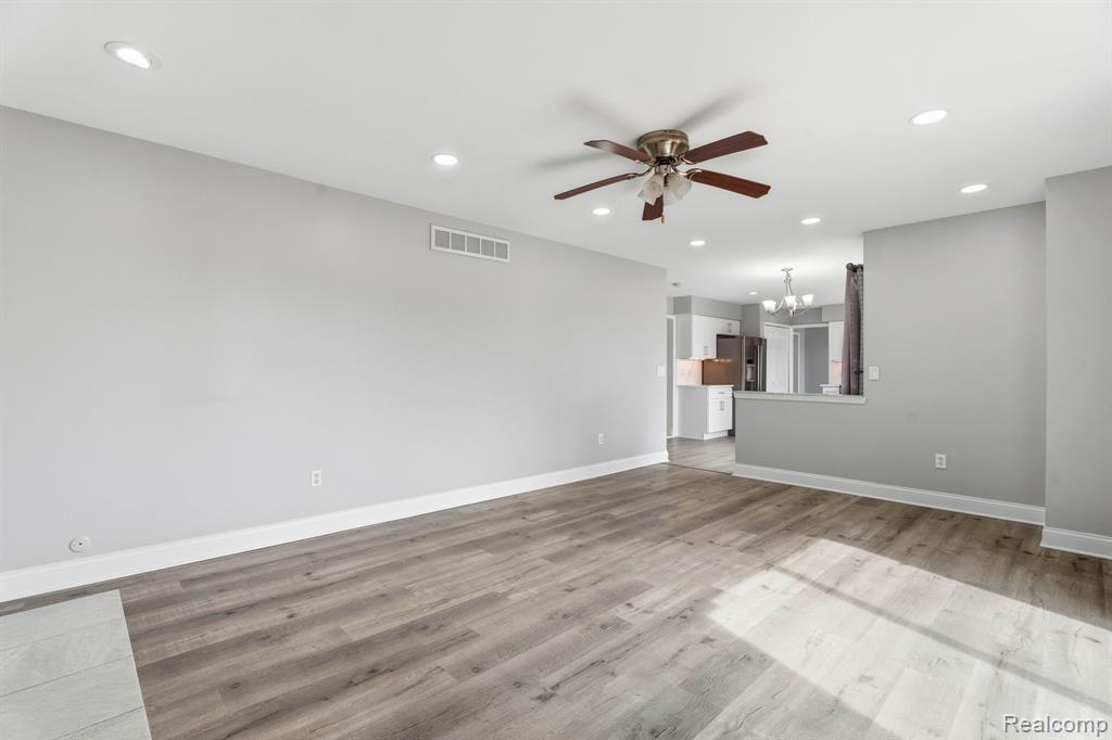 Unfurnished living room with ceiling fan, a chandelier, and light wood-style floors