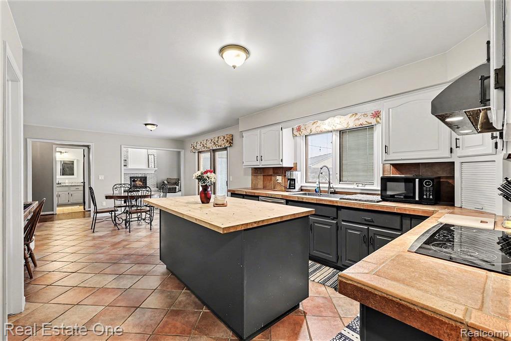 Kitchen featuring a kitchen island, decorative backsplash, white cabinets, gray cabinetry, and ventilation hood