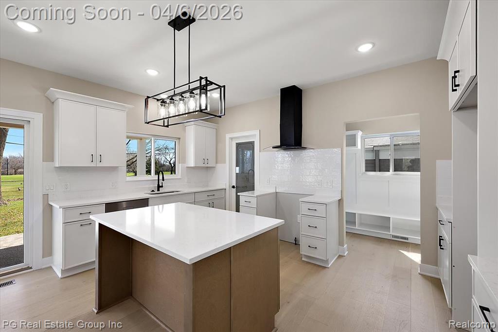 Kitchen featuring backsplash, a center island, light wood-type flooring, decorative light fixtures, and two tone cabinets