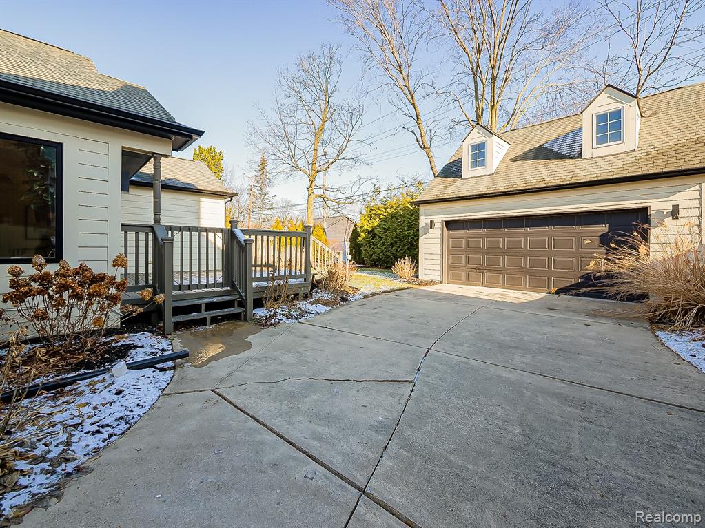 View of side of property with a wooden deck, a garage, concrete driveway, and a shingled roof