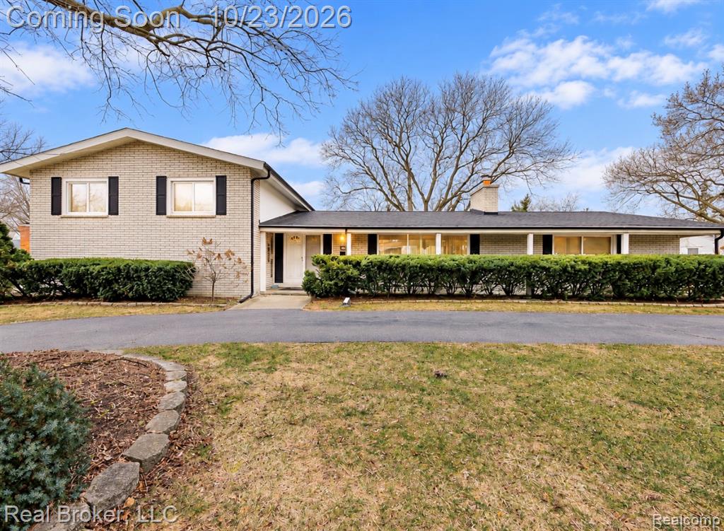 Single-story ranch exterior featuring masonry siding, a covered porch, a brick chimney, and a concrete driveway set on a landscaped lot