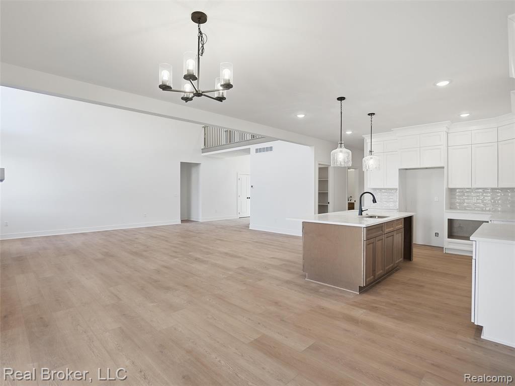 Kitchen with open floor plan, two tone cabinets, an island with sink, light wood finished floors, and backsplash