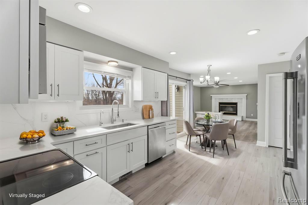 Kitchen featuring light wood-type flooring, stainless steel appliances, white cabinets, a high end fireplace, and open floor plan