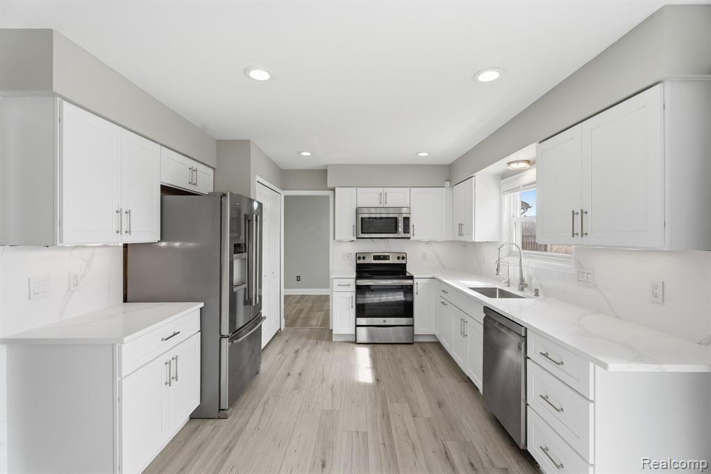 Kitchen featuring stainless steel appliances, white cabinets, recessed lighting, light wood-style flooring, and light stone countertops