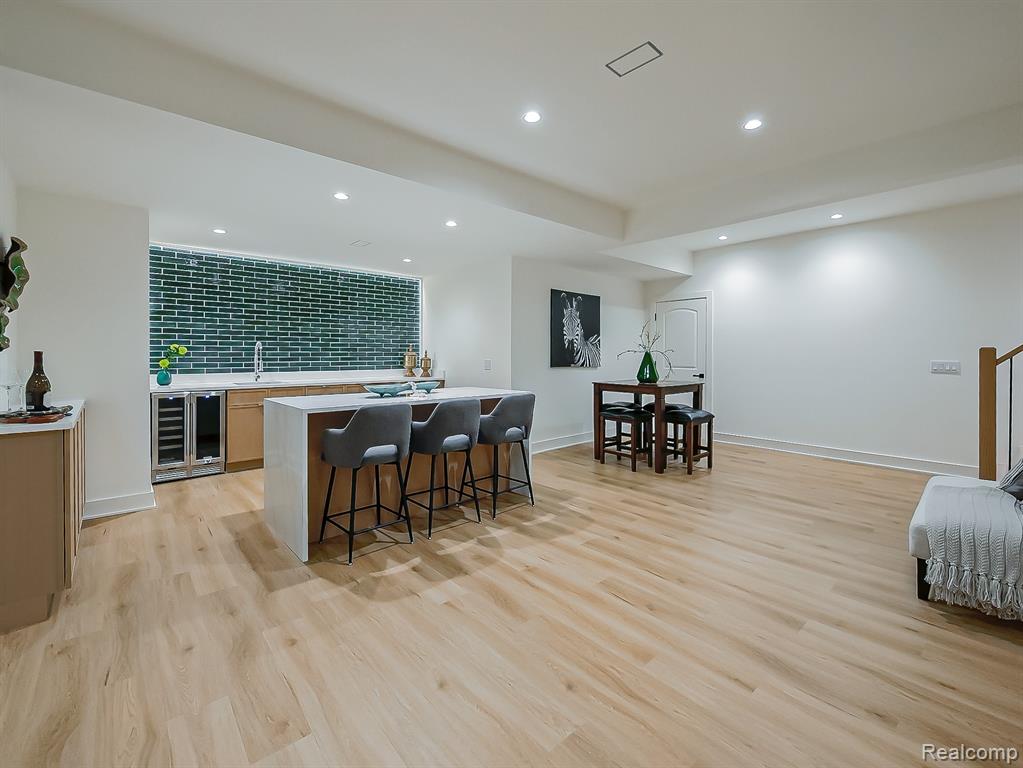 Indoor wet bar with wine cooler, light wood-style floors, light stone countertops, and recessed lighting