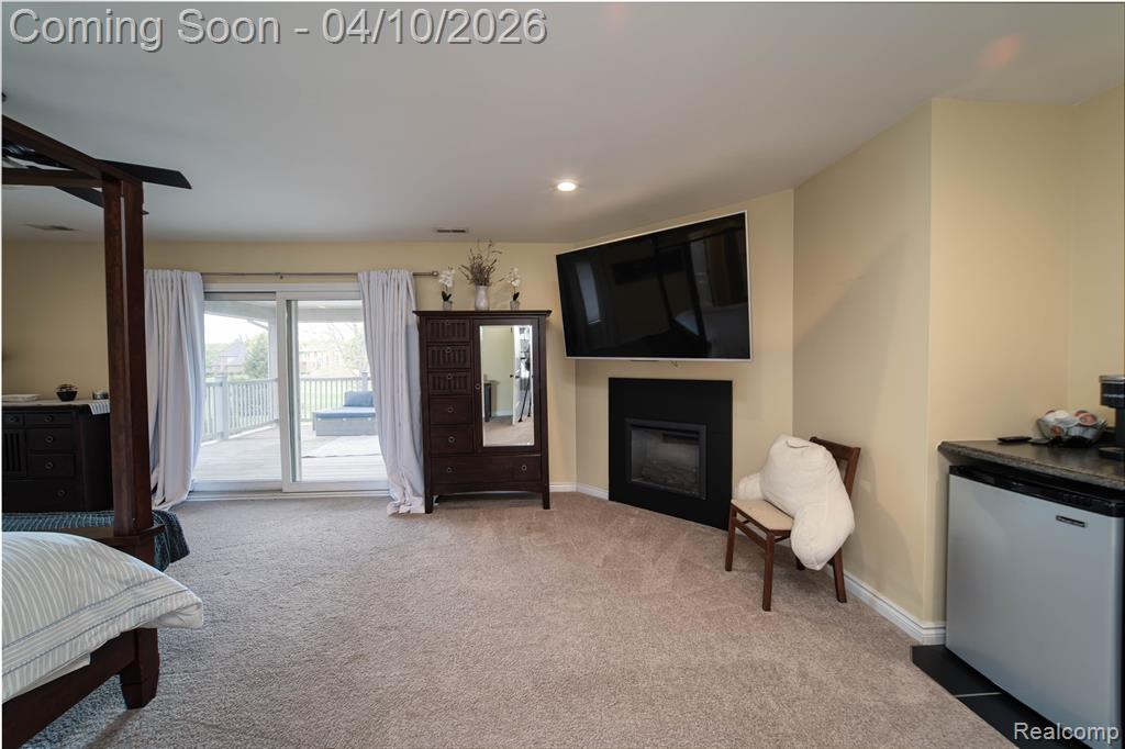 Bedroom with fridge, light colored carpet, access to outside, a glass covered fireplace, and recessed lighting