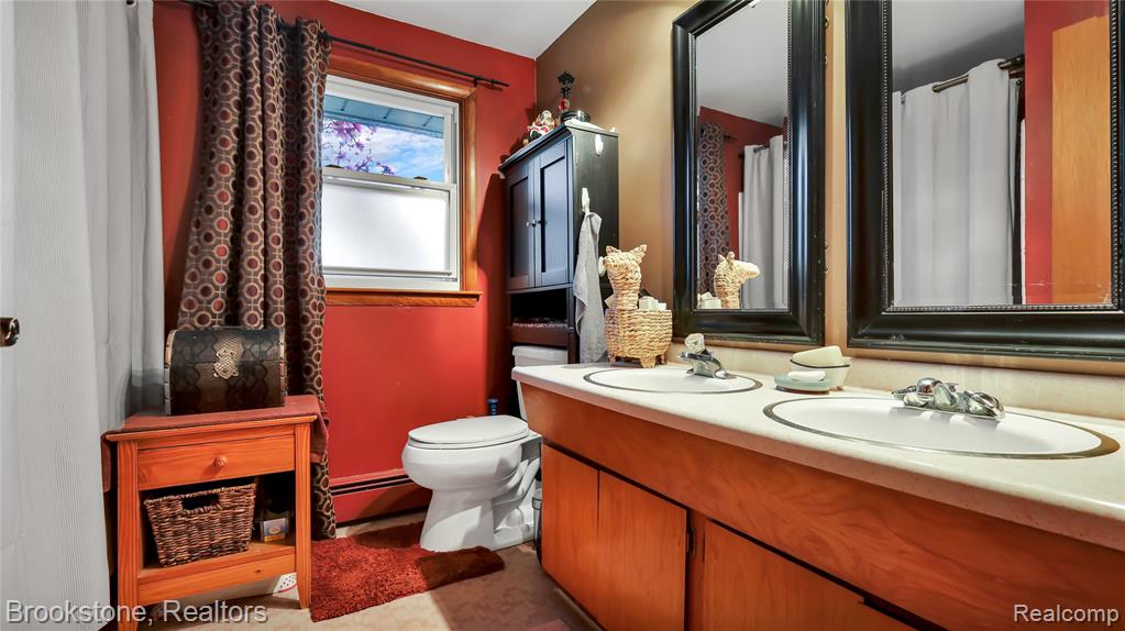 Bathroom featuring double vanity, baseboard heating, and curtained shower