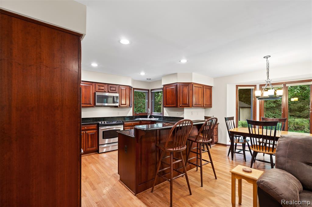 Kitchen with appliances with stainless steel finishes, dark stone countertops, a breakfast bar, pendant lighting, and light wood-style flooring