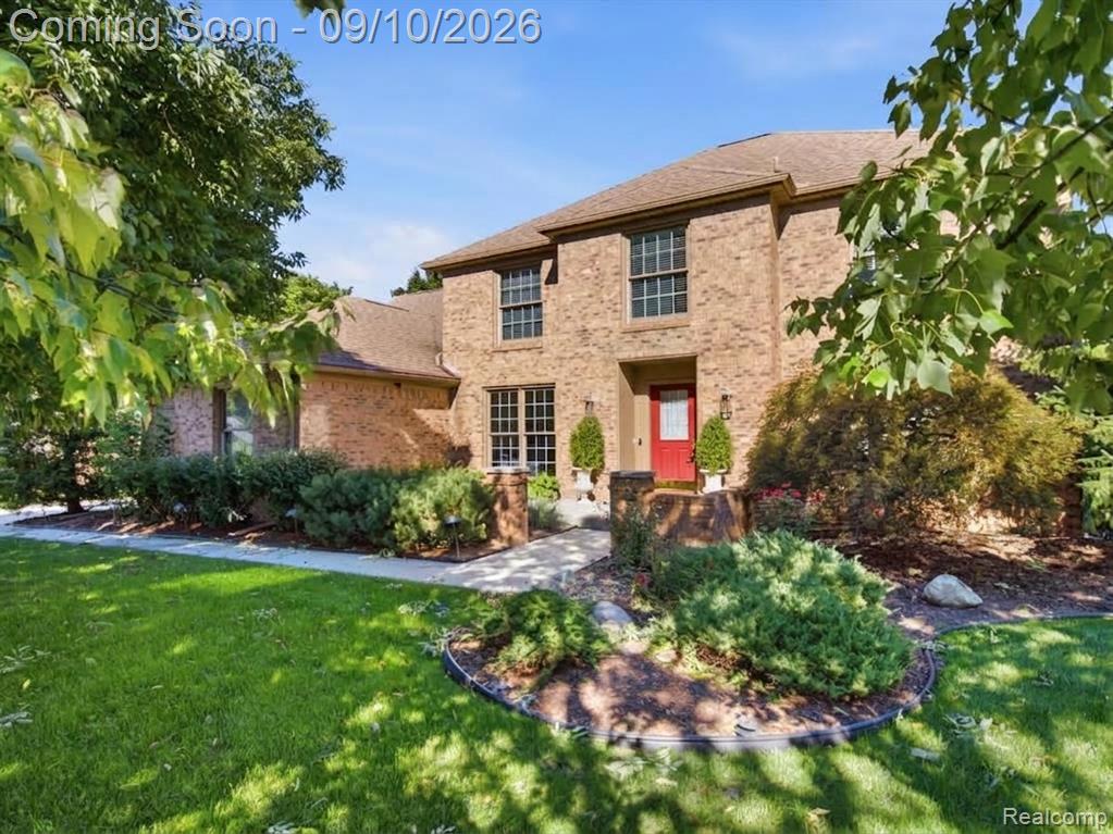 Brick exterior residence with a red front door, multiple windows, and extensive landscaping