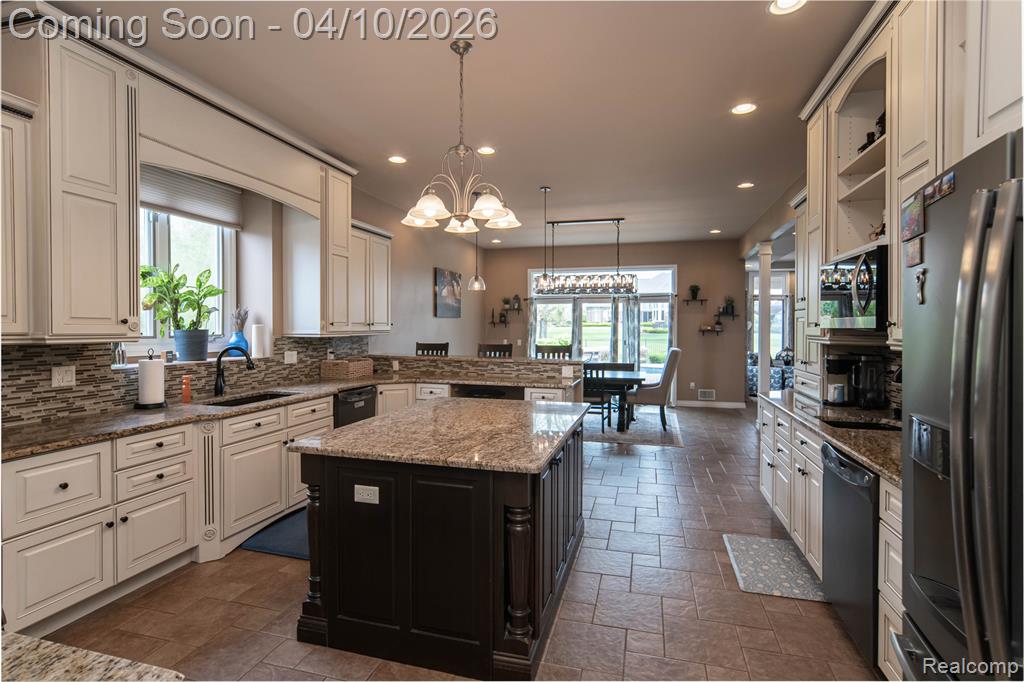 Dual tone kitchen with dual tone cabinets, stainless steel appliances, dark stone countertops, suspended lighting, and a center island