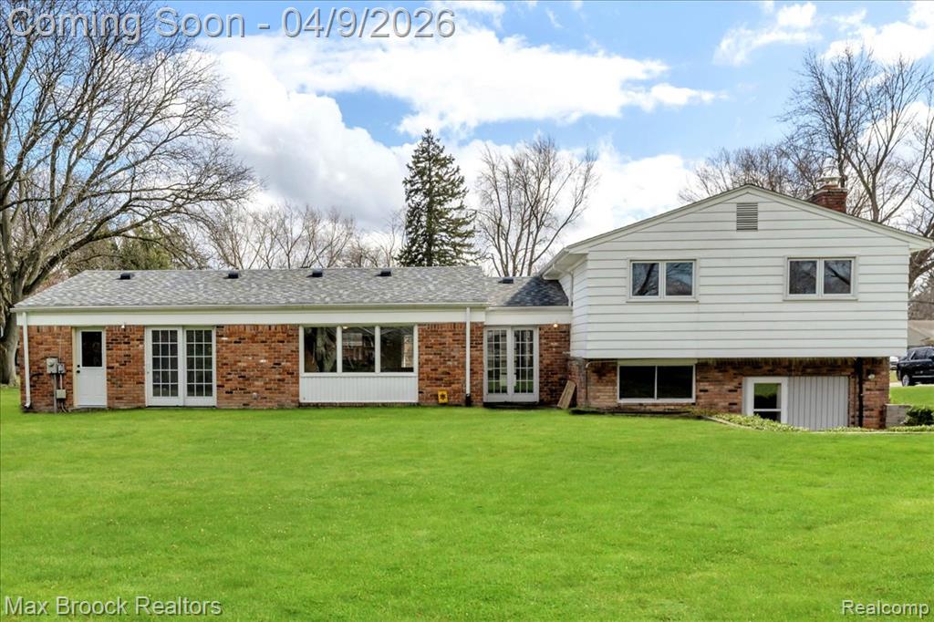 Rear view of property with french doors, brick siding, a lawn, a chimney, and a shingled roof
