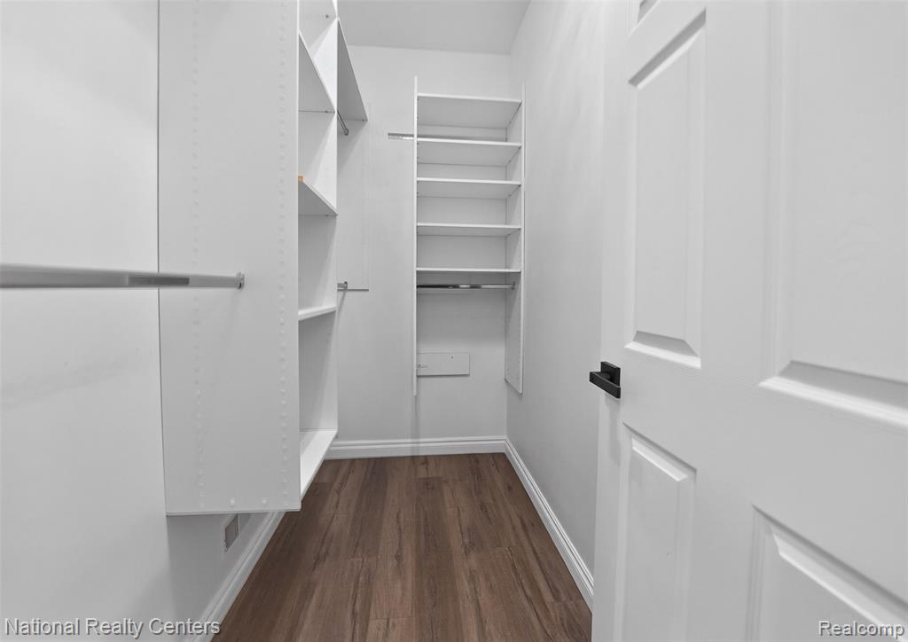 Walk in closet with dark wood-style floors