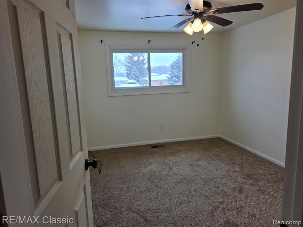 Carpeted spare room featuring a ceiling fan and baseboards