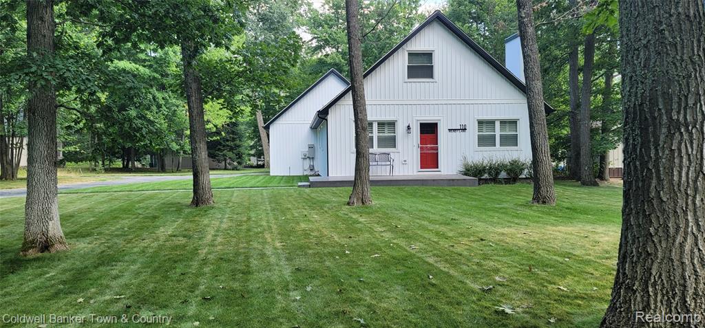 Modern farmhouse featuring a front yard, view of wooded area, and a chimney