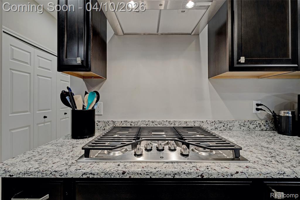 Kitchen with exhaust hood, stainless steel gas stovetop, light stone counters, and dark wood finish cabinetry